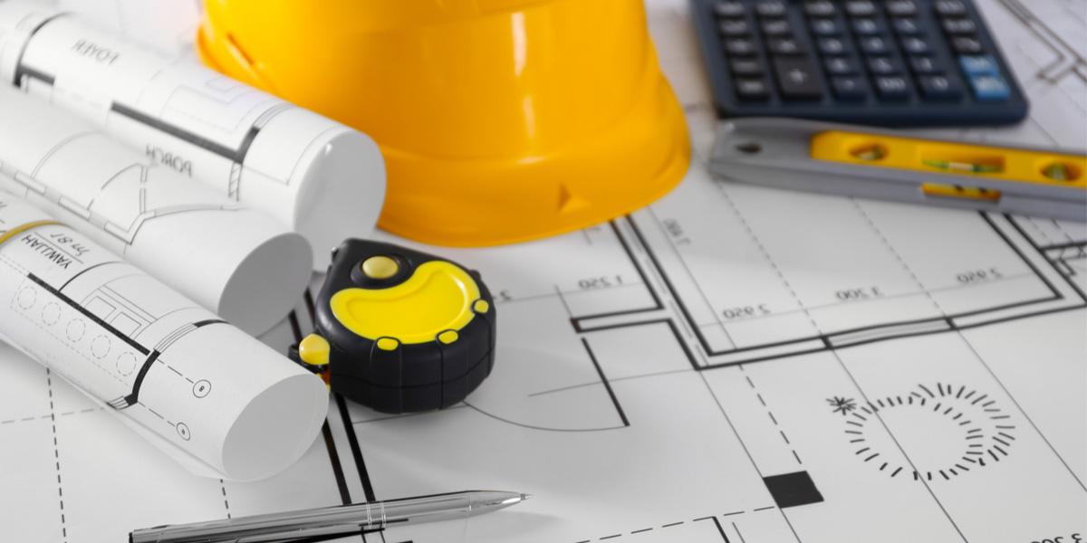 Blueprints, tape measure, hard hat and other tools on a table.